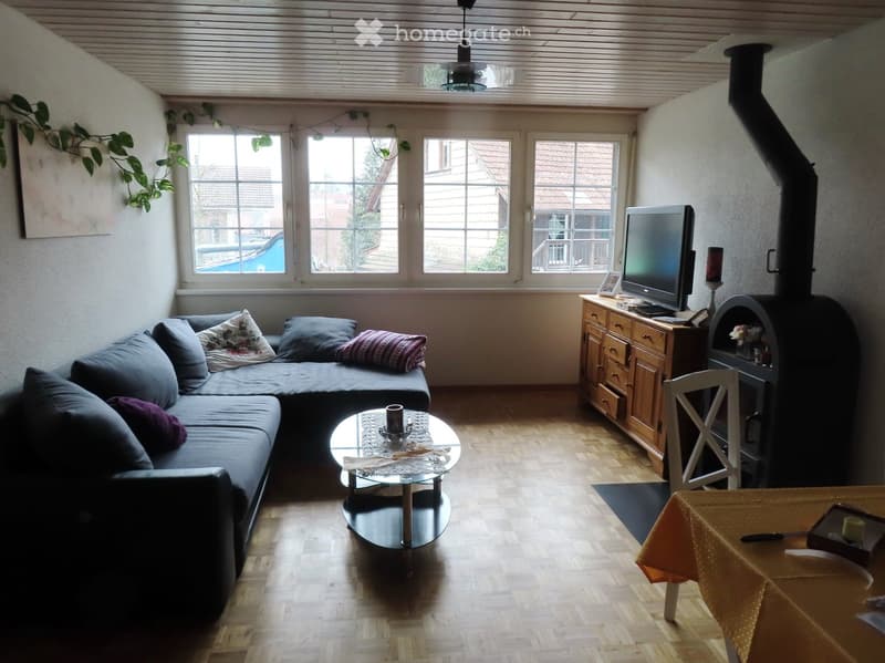 Living room with a grey sectional sofa, coffee table, television, fireplace, and wooden flooring.