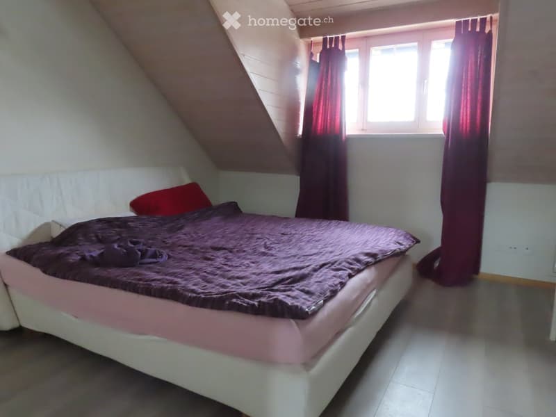 Cozy attic bedroom with a white bed, dark purple bedding, and red curtains on the windows.