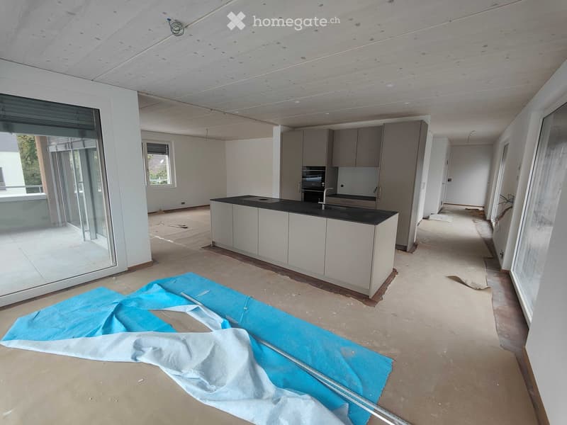 Modern kitchen with white cabinets, black countertop, and a sink. The floor is unfinished, and a blue protective sheet is on the floor.