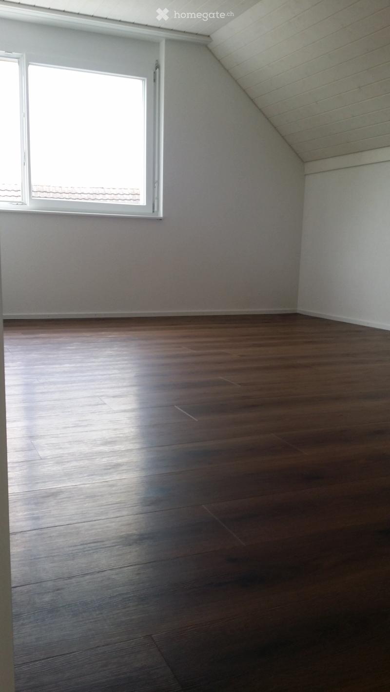 Empty room with wooden flooring and white walls, featuring a slanted ceiling and a single window letting in natural light.