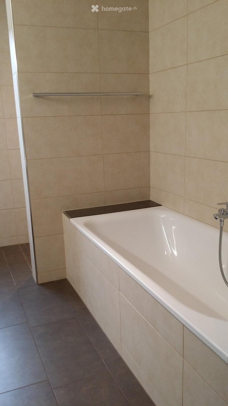 Modern bathroom with a white bathtub, beige tiled walls, and a chrome faucet.