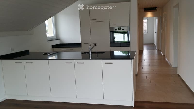 Modern kitchen with white cabinets, black countertops, a sink with a modern faucet, and an integrated oven. The space is bright with natural light from a window and has a hallway leading to another room.