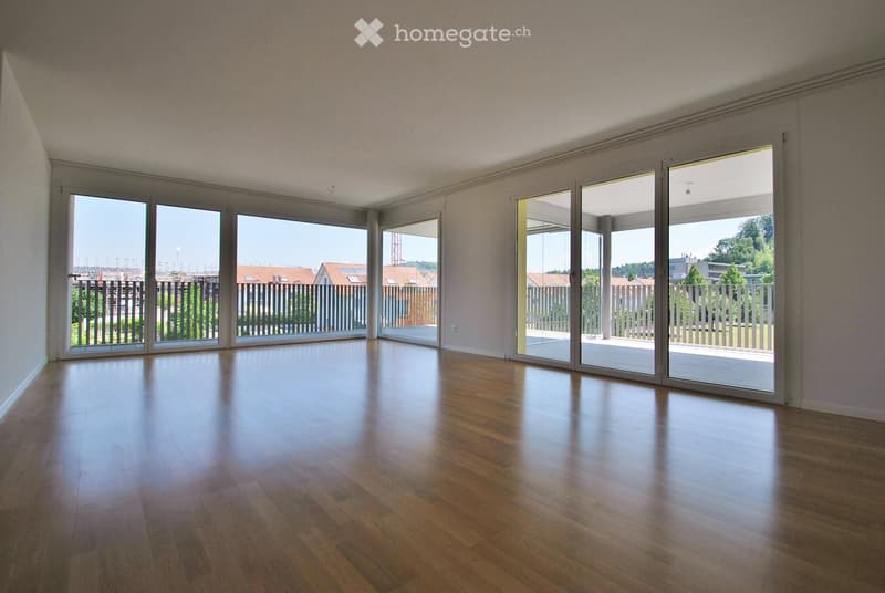 Empty room with wooden flooring and large sliding glass doors leading to a balcony or outdoor area. The walls are painted in a light color, and the space is well-lit with natural light.