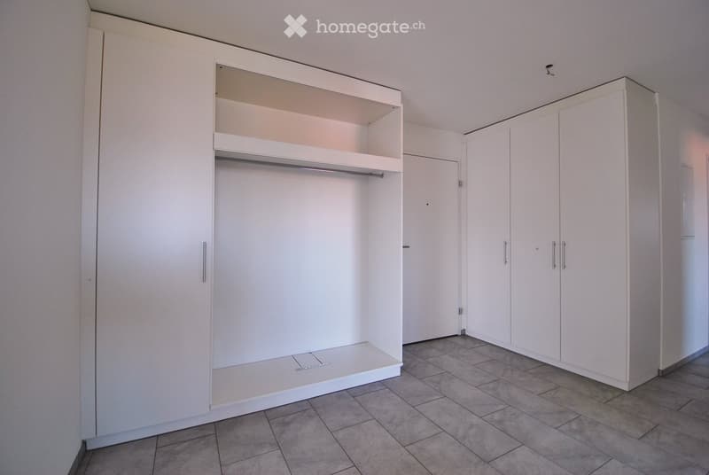 Empty room with white built-in wardrobes, tiled floor, and a small open closet area with a shelf and rod.