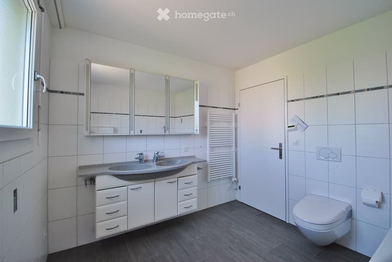 Modern bathroom with white tiles, a double sink, large mirror, white cabinetry, and a toilet.
