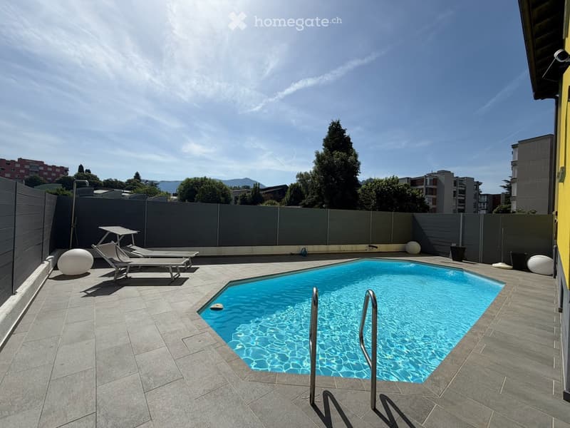Private outdoor area with a swimming pool, sun loungers, and decorative spheres, surrounded by a grey fence and trees.