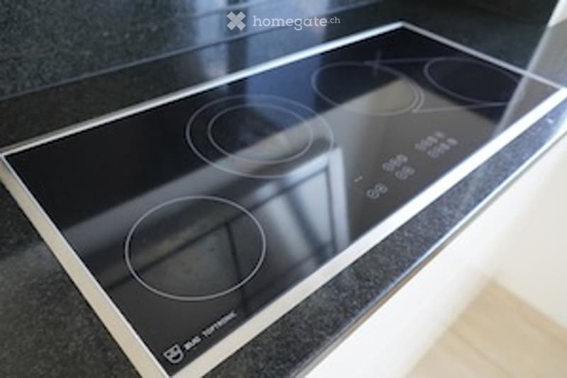 Modern induction cooktop with four circular cooking zones and control panel.