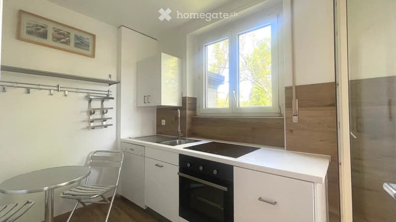 Modern kitchen with white cabinets, stainless steel appliances, a sink, stove, oven, and a small table with a chair.