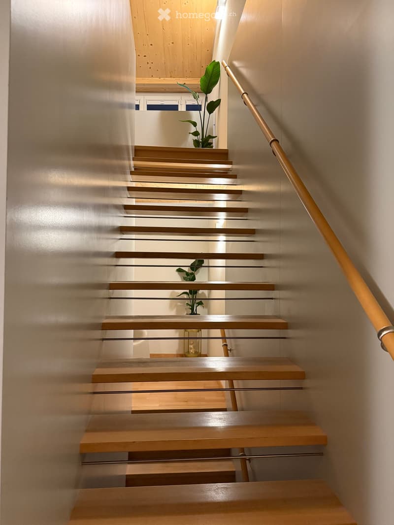 Modern staircase with wooden steps and a glass railing, featuring a sleek design and warm lighting.