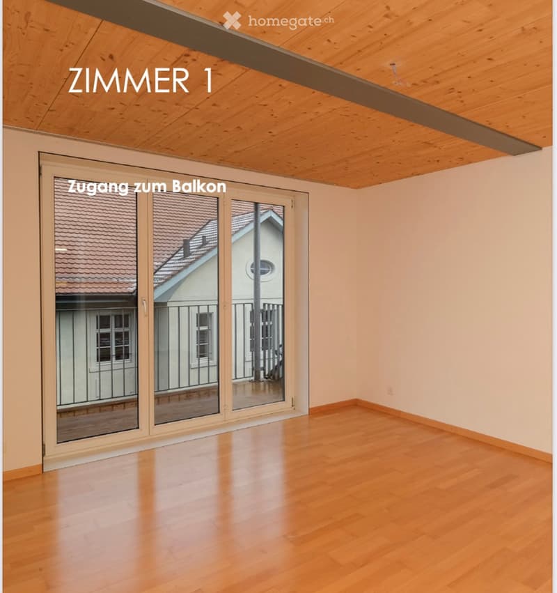 Empty room with wooden flooring, large sliding glass door leading to a balcony, and exposed wooden ceiling beams.