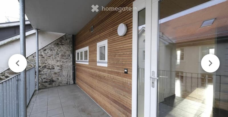 Balcony with wooden paneling, tiled floor, glass door leading inside, and a stone wall on one side.