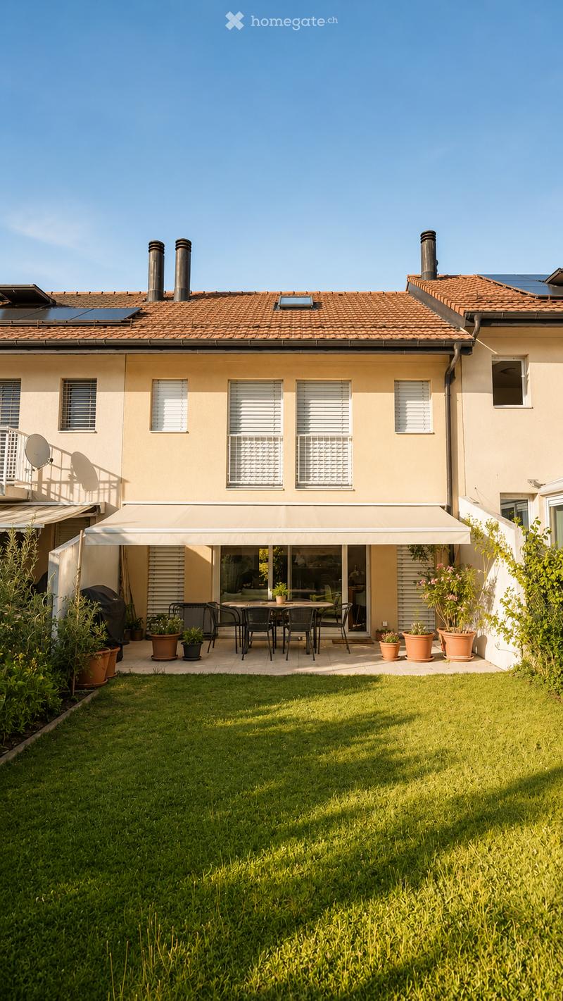 A well-maintained garden with a neatly trimmed lawn, a patio area with a dining set, and potted plants. The house features a tiled roof, multiple windows, and a covered outdoor seating area.