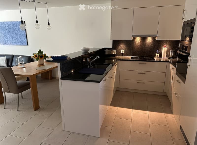 Modern kitchen with white cabinets, black countertops, and a central island. Includes a dining area with a table, chairs, and a sofa. Appliances such as a microwave, oven, and toaster are visible, along with a sink and faucet.