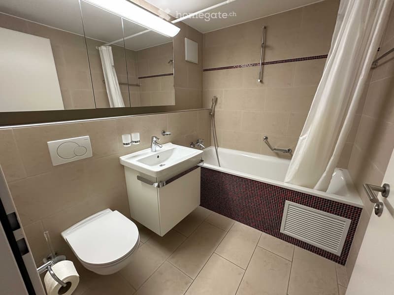 Modern bathroom with beige tiles, a white sink, toilet, bathtub, and a large mirror above the sink.