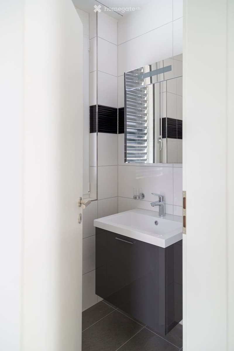 Modern bathroom with white tiles, black accents, a white sink, a large mirror, and a sleek faucet.