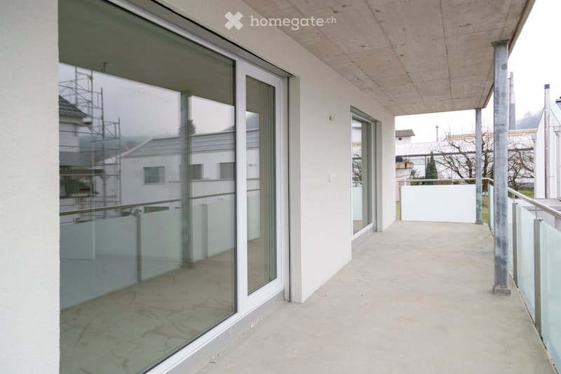 Modern balcony with large glass sliding doors, concrete floor, and metal railings, overlooking a residential area.