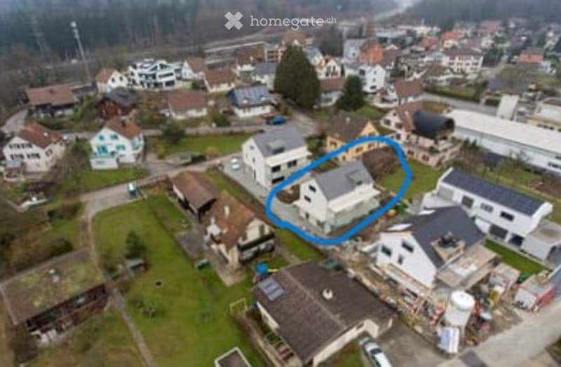 Aerial view of a residential area with multiple houses, surrounded by greenery and other structures.