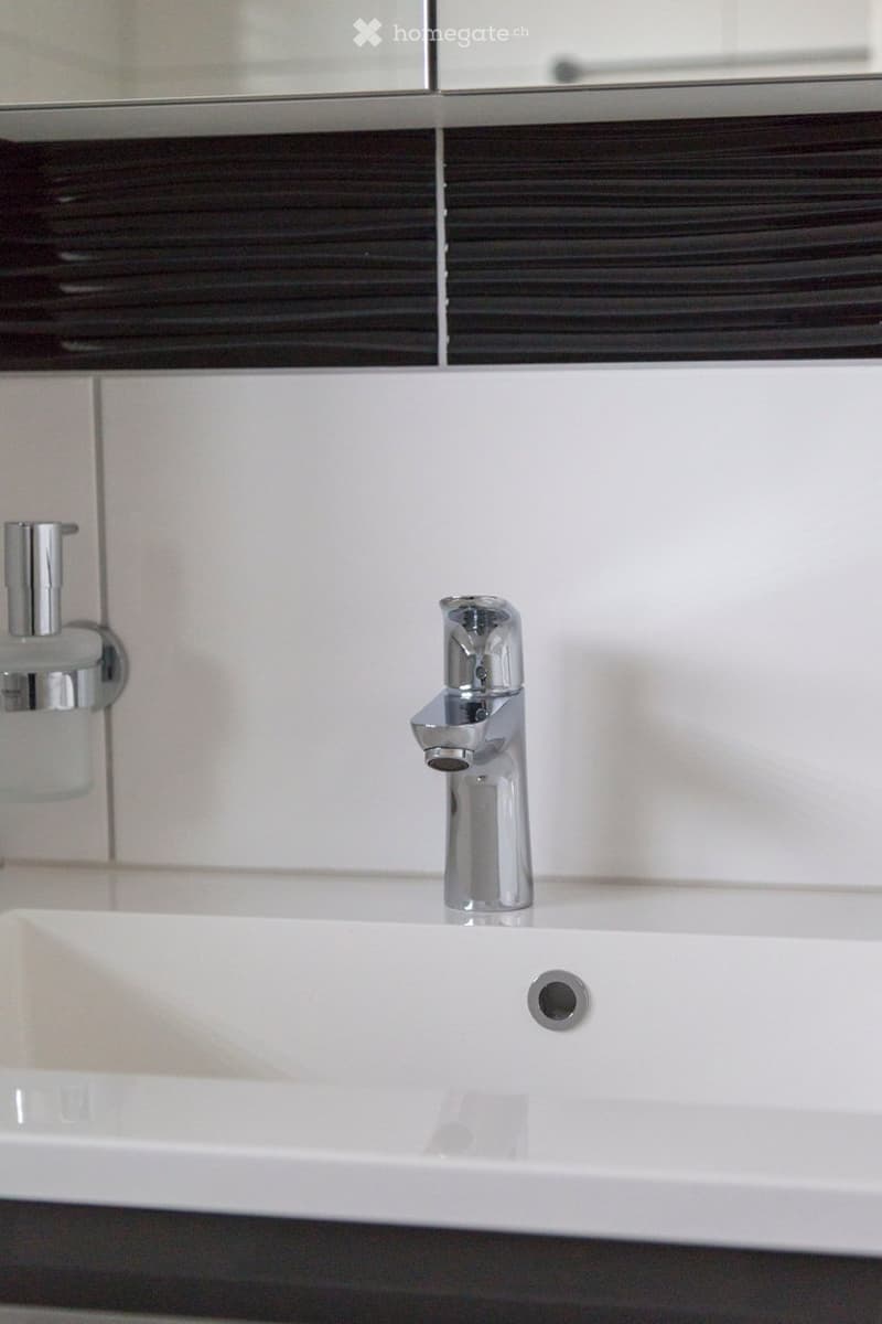 Modern bathroom sink with a sleek chrome faucet and a soap dispenser mounted on the wall.