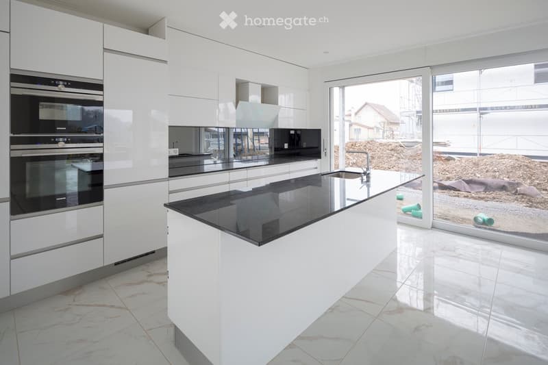 Modern kitchen with white cabinets, black countertops, built-in ovens, and a central island with a sink and faucet.