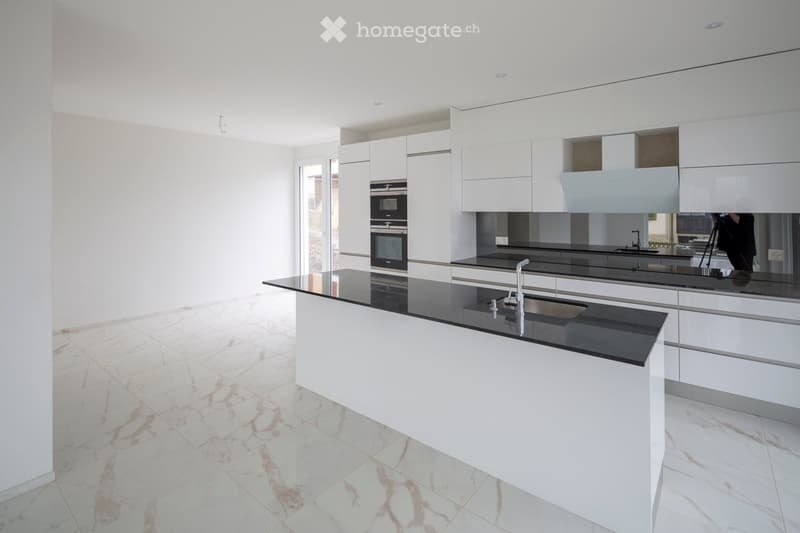 Modern kitchen with white cabinets, black countertops, and a central island. Features a built-in oven and a sink with a modern faucet.