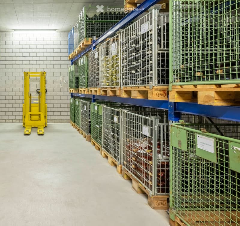 Warehouse with multiple rows of metal cages containing bottles, stacked on pallets, and a yellow forklift in the foreground.