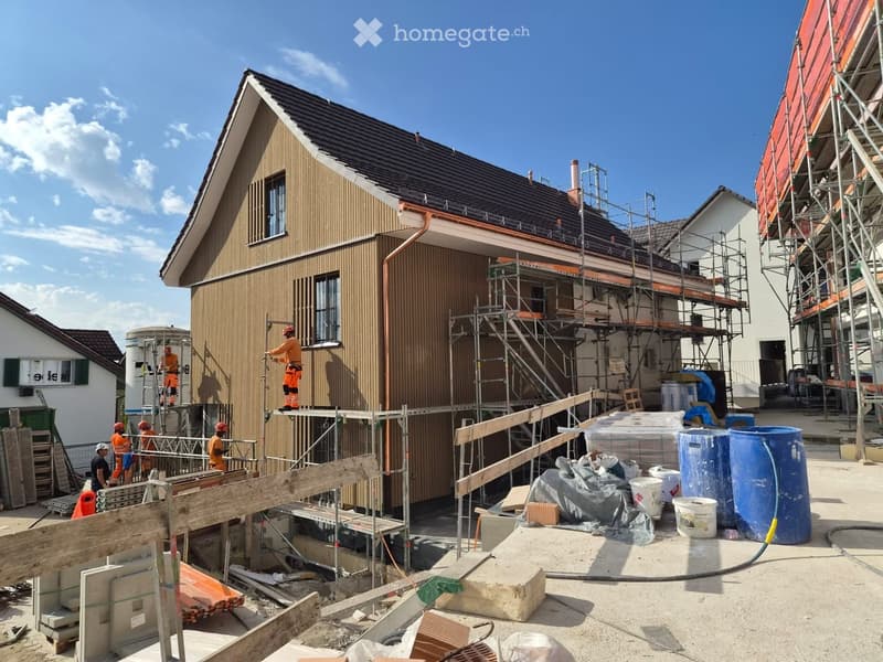 A partially constructed house with scaffolding, workers in safety gear, and construction materials scattered around.