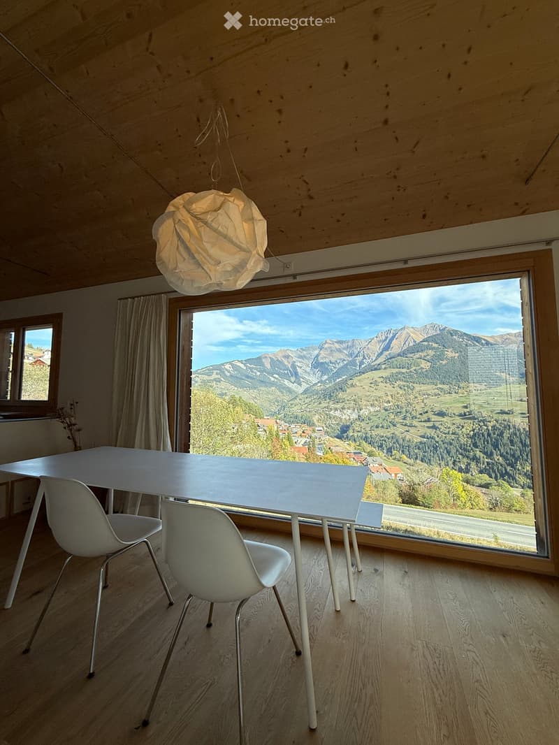 Bright dining area with a white table and chairs, large window offering a scenic mountain view.