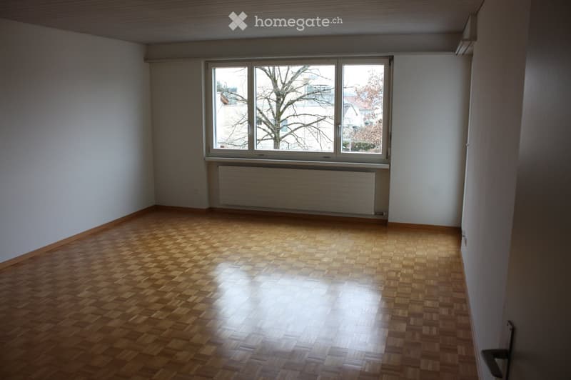 Empty room with wooden flooring, white walls, and a large window with a radiator below it.