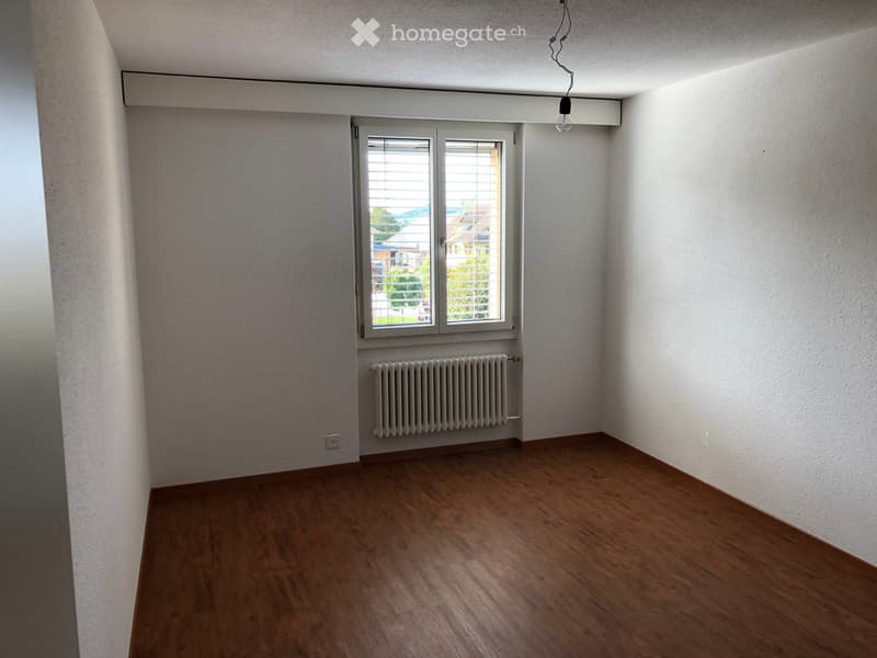 Empty room with wooden flooring, white walls, a window with blinds, and a radiator below the window.