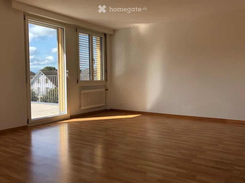 Empty room with wooden flooring, large sliding glass door, radiator, and window with blinds.