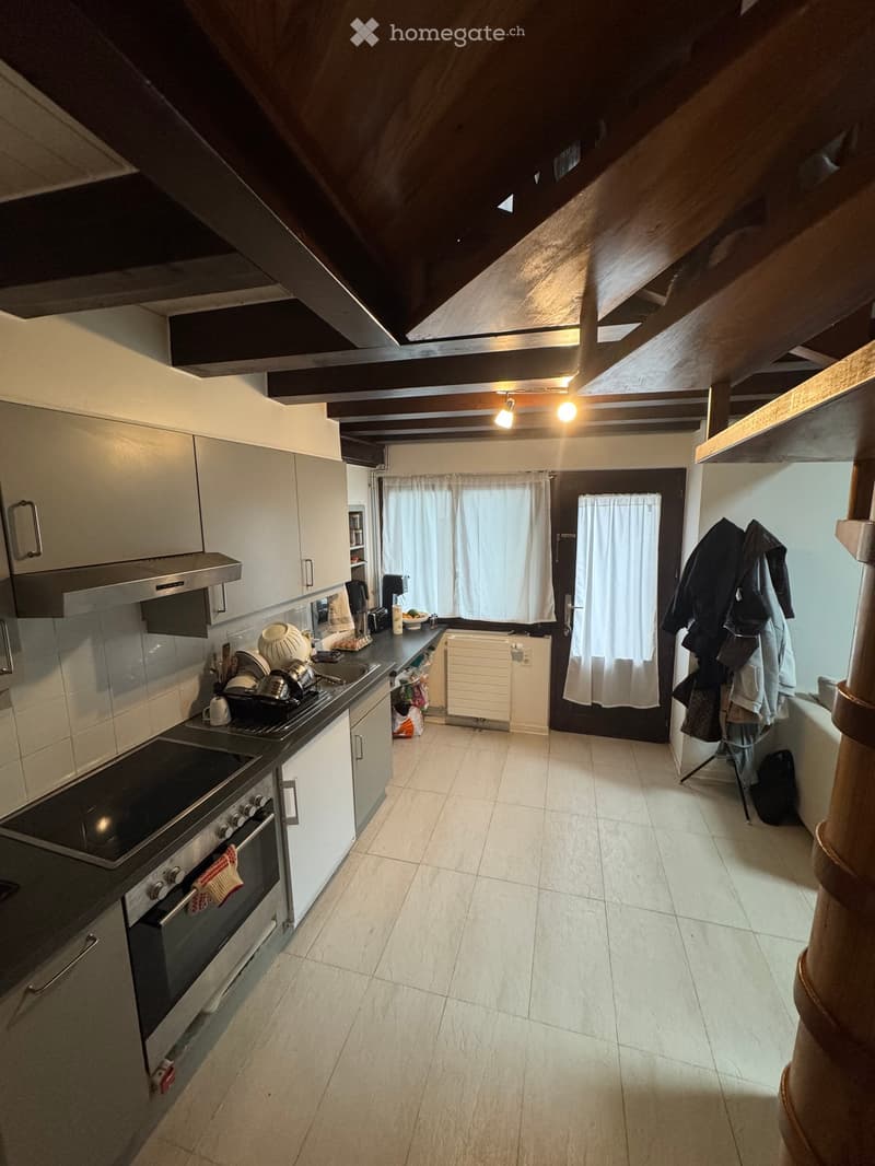 Modern kitchen with white cabinets, stainless steel appliances, and a tiled floor. Features an oven, stove, sink, and various kitchen items on the counter.