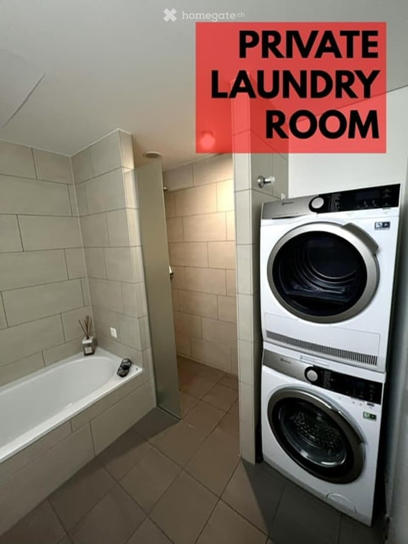 Bathroom with a bathtub, tiled walls, and a private laundry area featuring a washing machine and dryer.