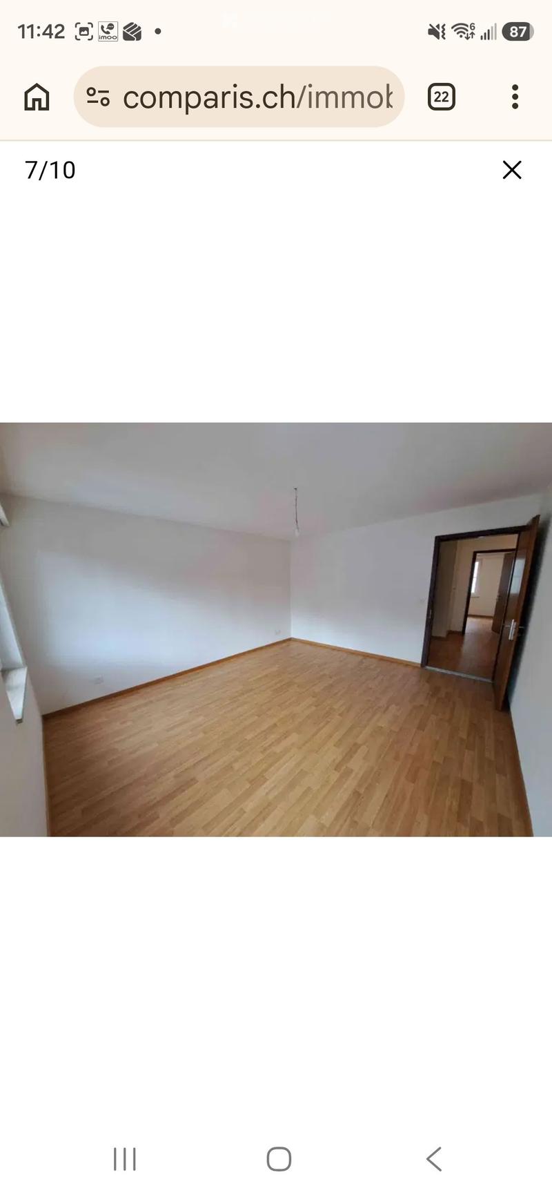 Empty room with wooden flooring and white walls, featuring a doorway leading to another room.
