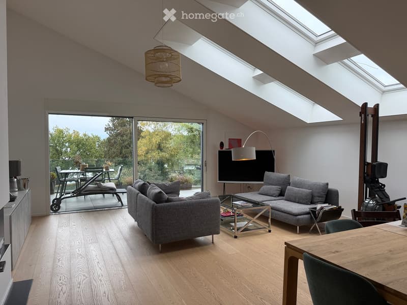 Modern living room with grey sofa, coffee table, dining table, chairs, TV screen, and a large window with a view of the garden.