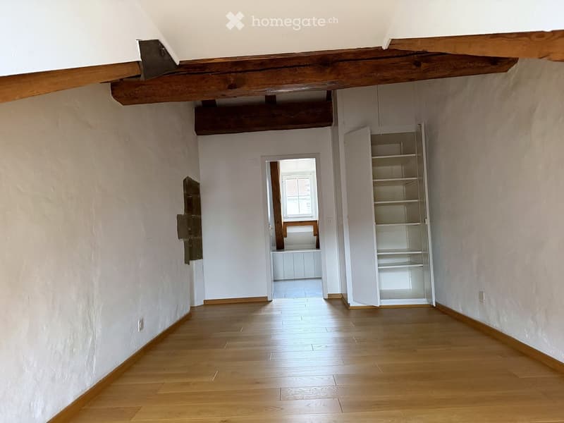 Empty hallway with wooden flooring, white walls, exposed wooden beams, and an open closet with empty shelves.