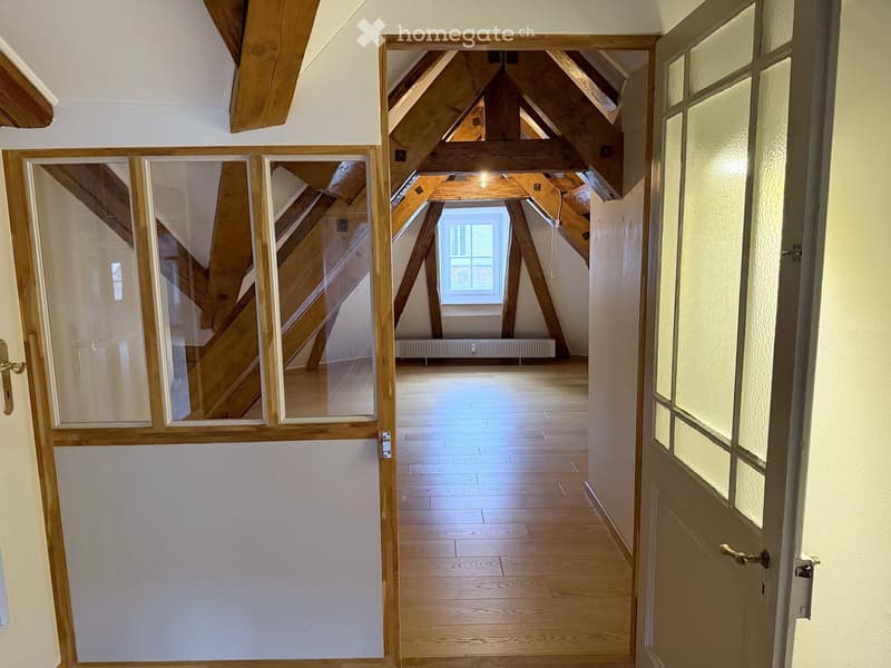 Bright, wooden-floored hallway with exposed wooden beams and a skylight at the end, leading to an open attic space.