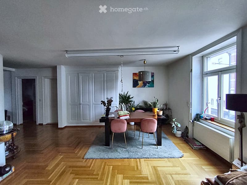 Bright, open dining area with wooden herringbone flooring, a dining table with pink chairs, a floor lamp, and a mirror on the wall.
