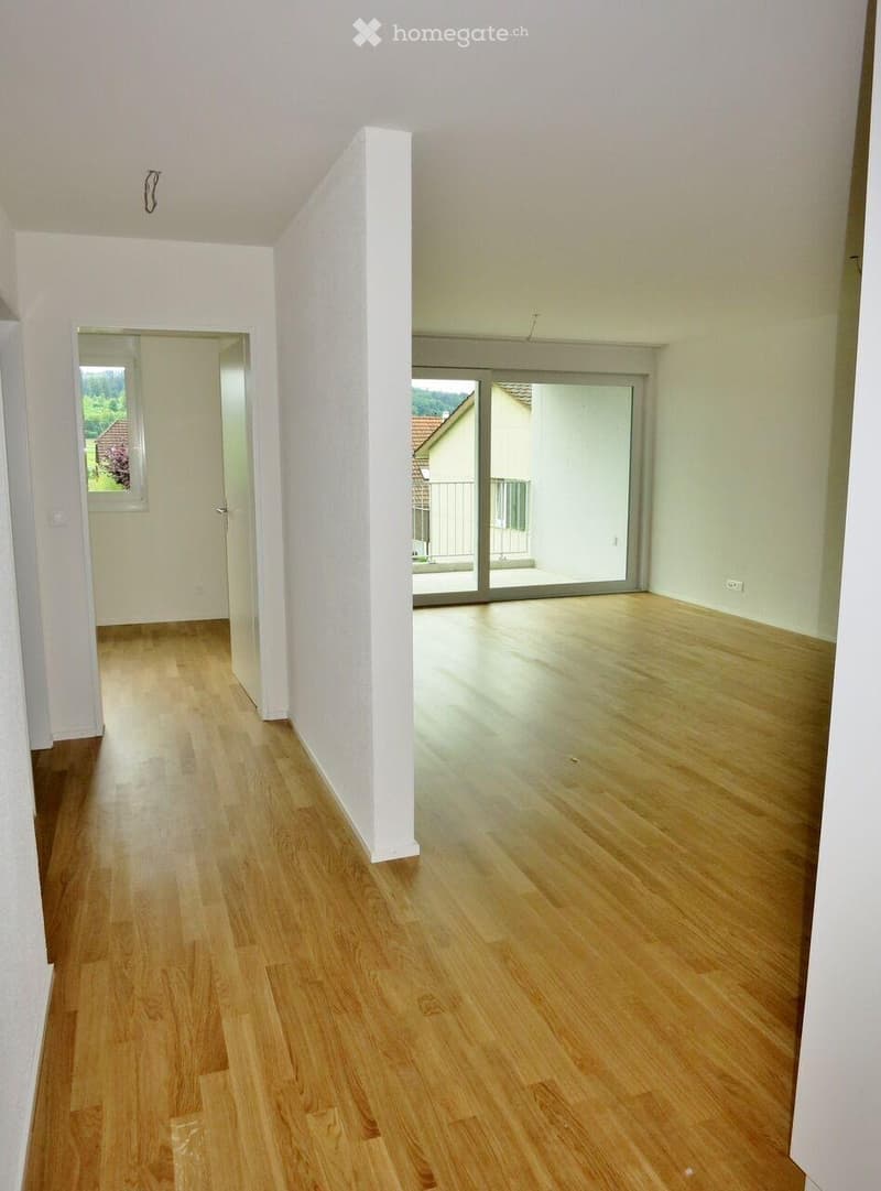 Empty room with light wooden flooring, white walls, and a sliding glass door leading to a balcony.