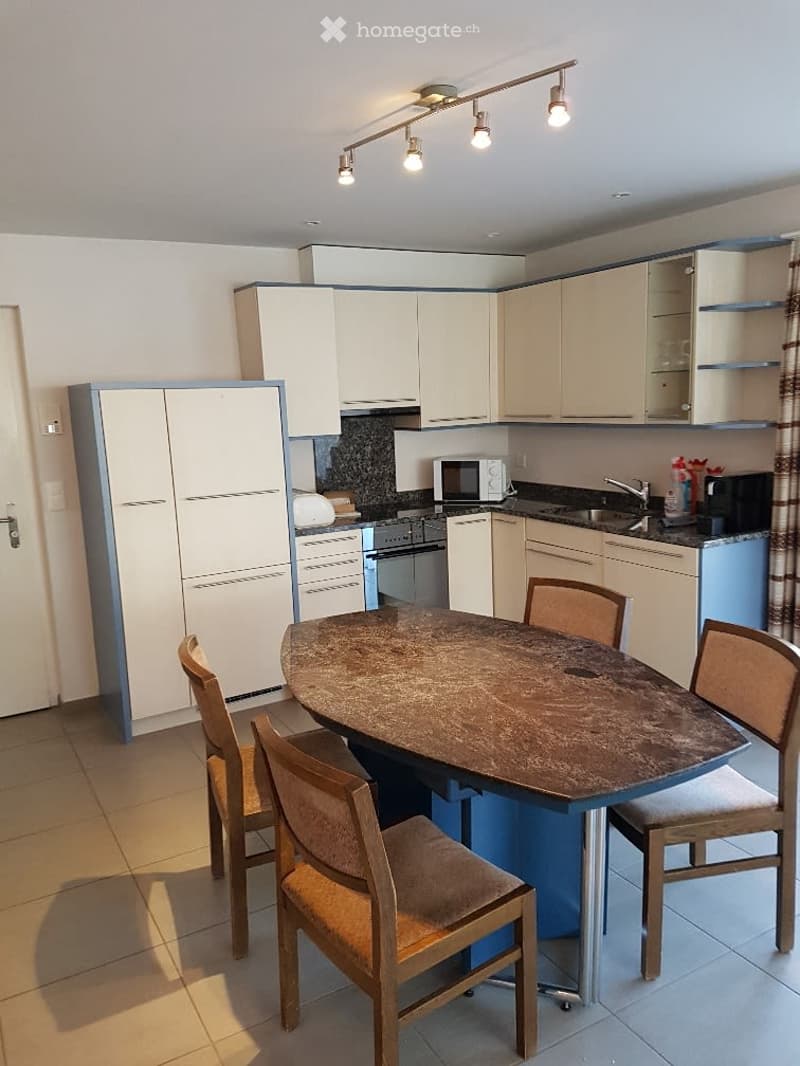 Modern kitchen with white cabinets, a round dining table with four chairs, a microwave, and a sink with a faucet.