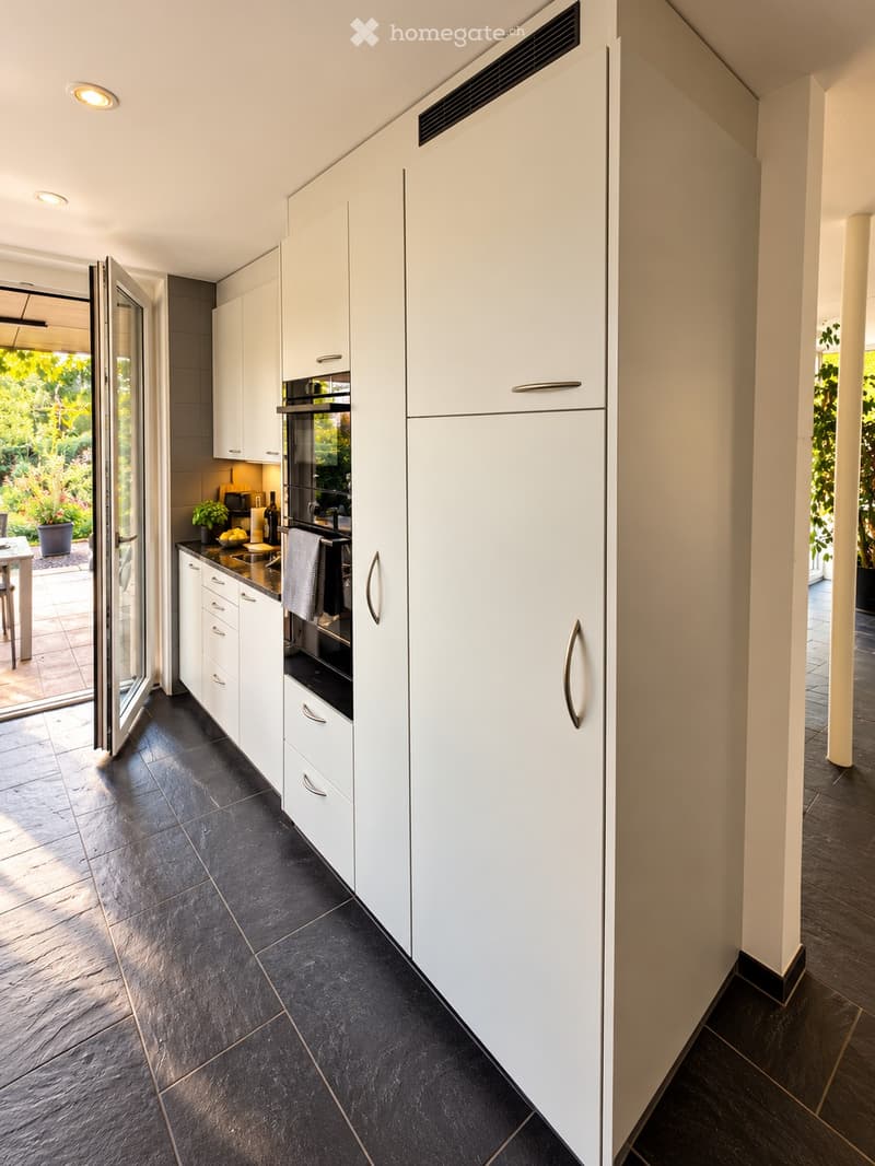 Modern kitchen with white cabinets, black tiled floor, and stainless steel appliances. Features an open sliding door leading to a garden area.