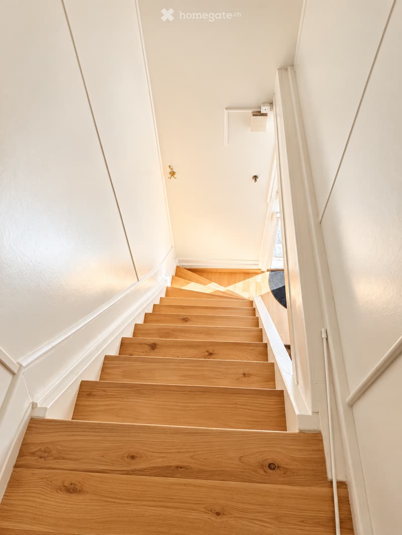 A modern staircase with wooden steps and white walls, featuring a curved design and a handrail on one side.