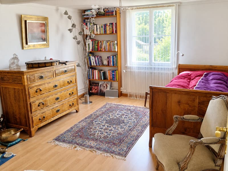 Cozy bedroom with wooden bed, dresser, bookshelf, and a patterned rug on the floor.