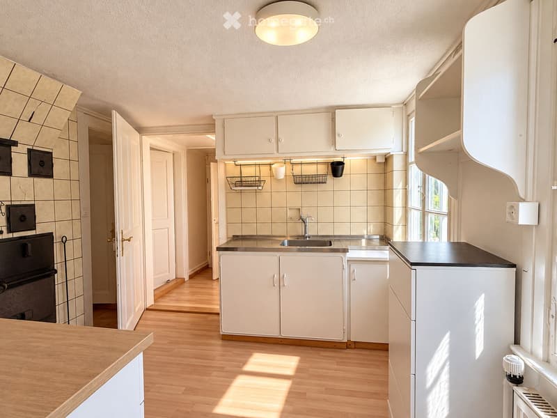 Bright kitchen with white cabinets, wooden flooring, and a stainless steel sink. Features an oven, refrigerator, and a window letting in natural light.