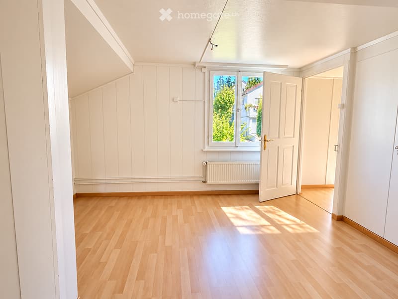Empty room with wooden flooring, white walls, and a window with a view of greenery. No furniture or equipment is present.