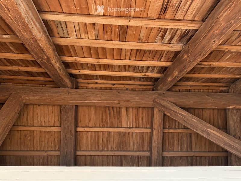 An unfurnished room with exposed wooden beams and a wooden ceiling structure, showing the raw construction details of the interior.