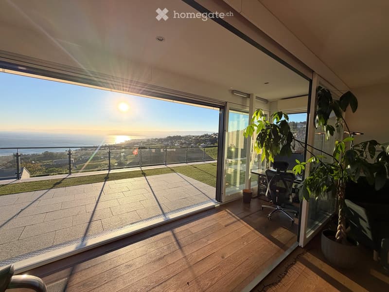 Bright room with wooden flooring, large glass doors opening to a balcony with ocean view, featuring a chair, small table, and potted plant.
