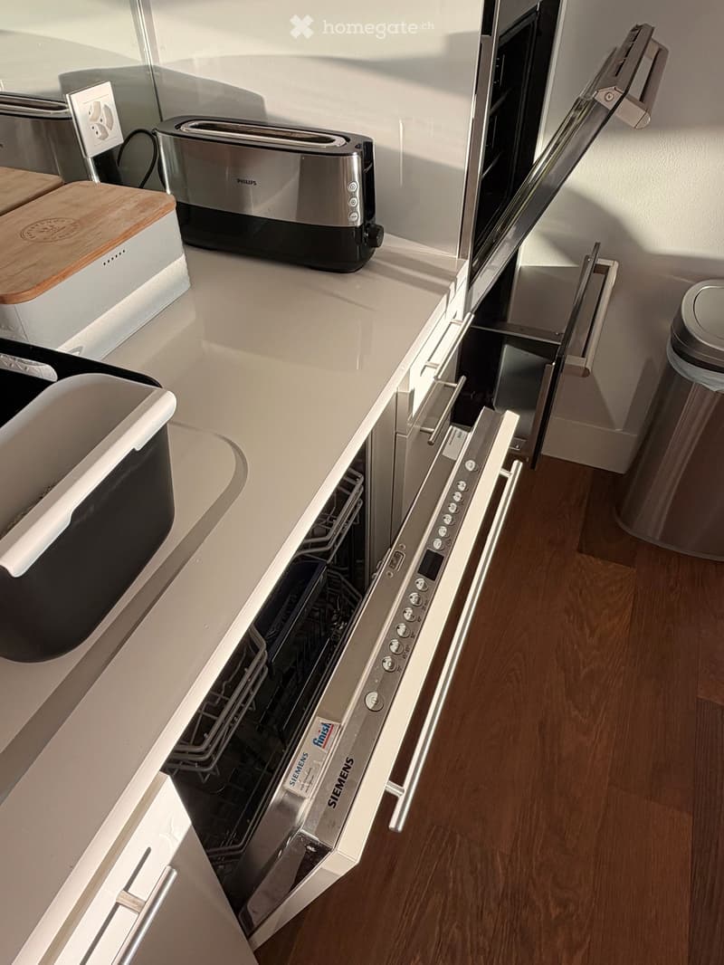 Modern kitchen with white countertops, a stainless steel Siemens dishwasher, a Philips toaster, and a wooden cutting board on the counter.