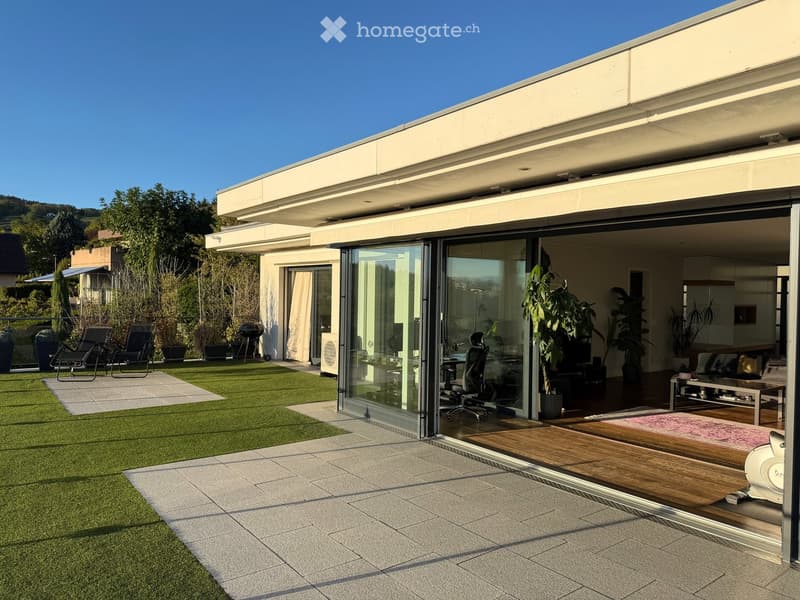 Modern outdoor patio with artificial grass, tiled flooring, lounge chairs, and a view of the surrounding landscape.