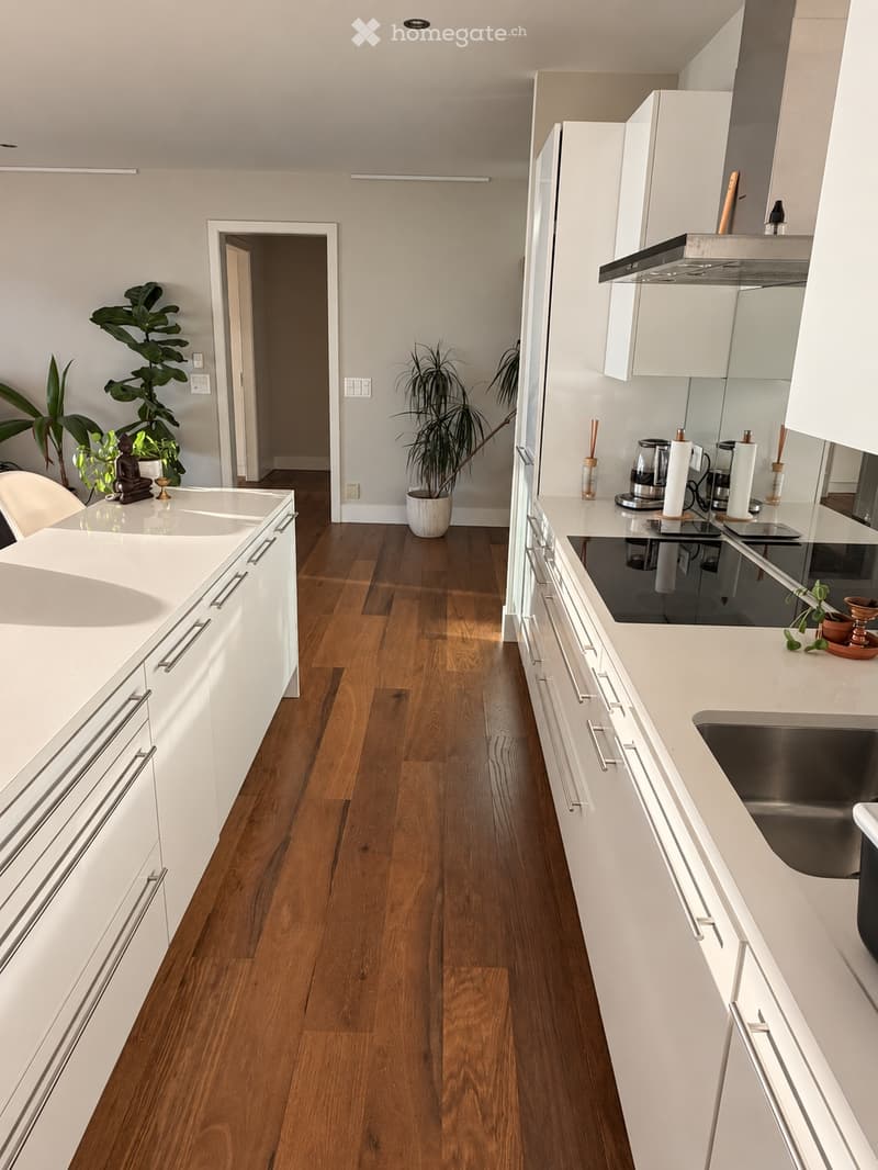 Modern kitchen with white cabinets, wooden flooring, stainless steel appliances, and a central island with a sink and countertop.