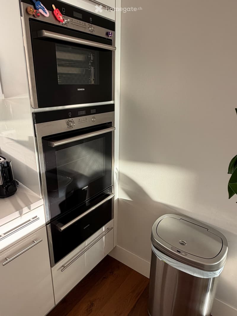 Modern kitchen with built-in Siemens ovens, a stainless steel trash bin, and a coffee maker on the counter.